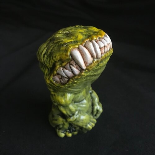 A small figurine. This creature, though humanoid, has no eyes, and its unnaturally large head is defined only by a large, closed mouth with teeth bared. It sits on its hind legs, docile, its head tilted upwards. This version of the doll is a spring green..