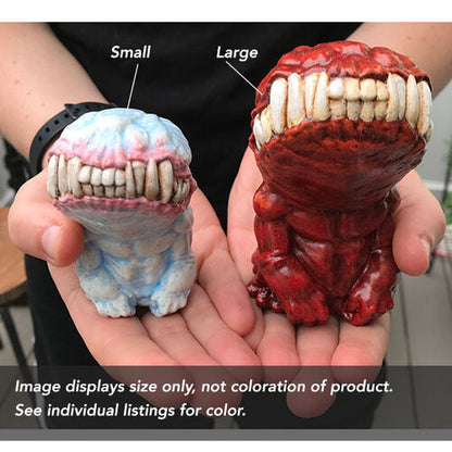 Two figurines held in a person's hand. One figurine is about 2/3 of the size of the other. Text boxes point to the left and caption it "small" and caption the right one "large." The bottom text reads, "Image displays size only, not coloration of product. See individual listings for color."